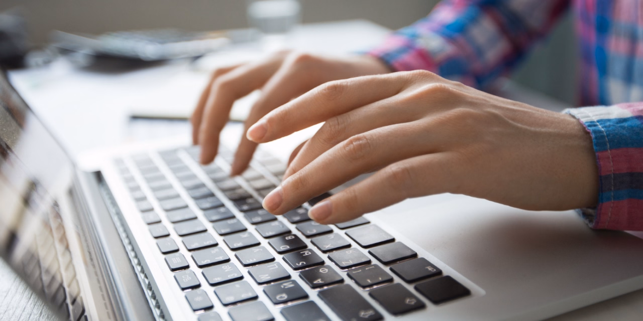 Dłonie osoby w kraciastej koszuli piszącej na klawiaturze laptopa