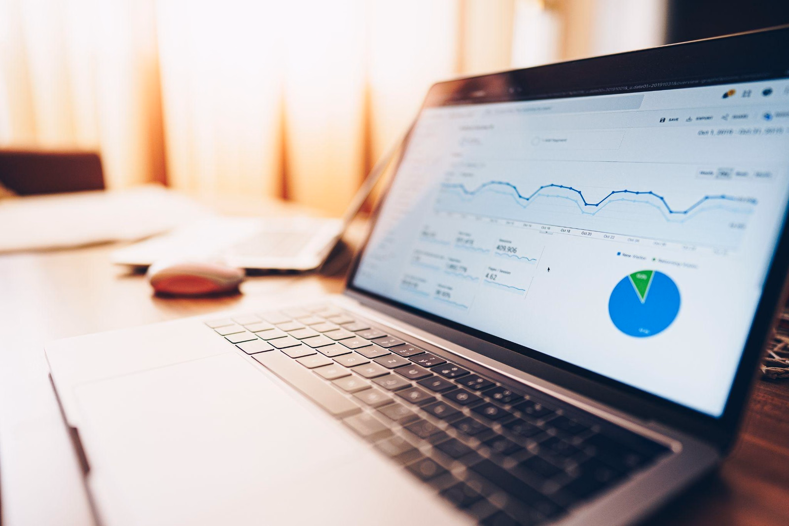 Laptop na biurku z otwartym panelem Google Analytics – wykres liniowy ruchu i wykres kołowy statystyk strony